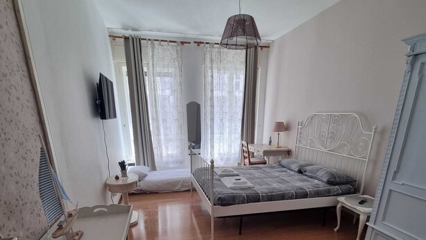 A bedroom with a bed, a desk, a chair, a TV, and a window with curtains.