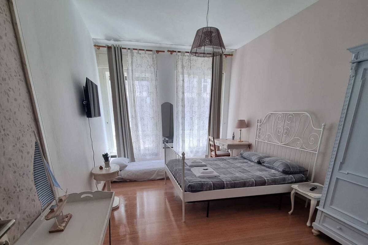 A bedroom with a bed, a desk, a chair, a TV, and a window with curtains.