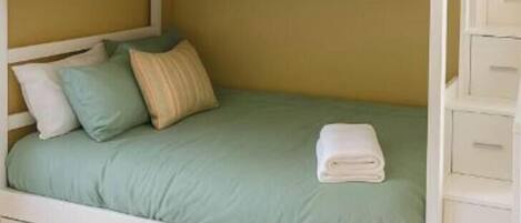 A bunk bed with a green mattress, white bedding, and a white drawer unit.