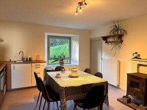 A compact kitchen with a dining area, a window with a view of greenery, and a hanging plant.