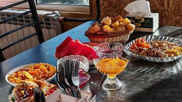 Uma mesa de jantar com diversos alimentos, utensílios, um cesto de pão e uma caixa de lenços.