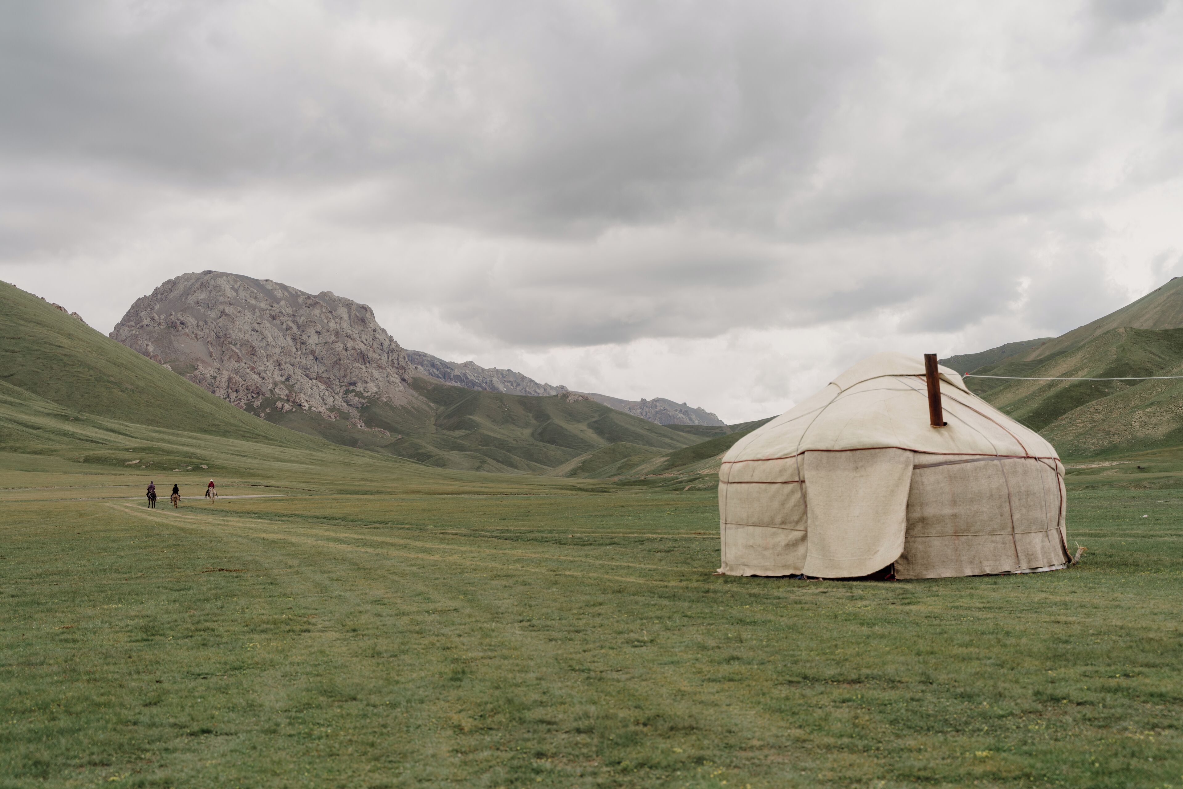 A yurt in a grassy field with mountains in the background.