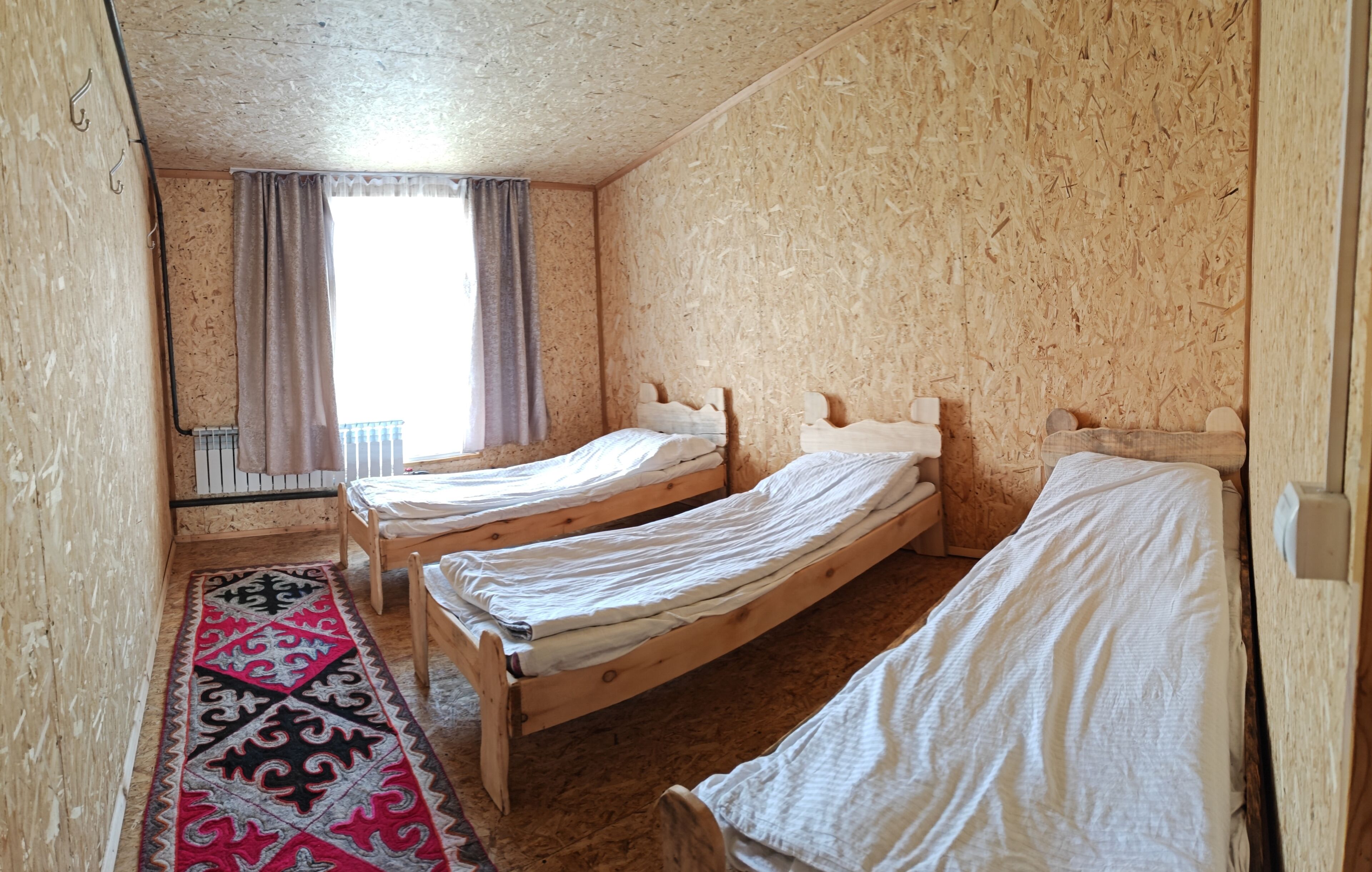 A room with three wooden beds, a patterned rug, and a window with curtains.
