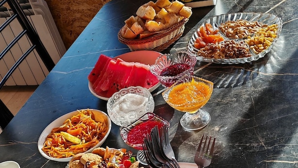 Une table à manger avec divers plats et ustensiles, un panier de pain et une vue sur le paysage par la fenêtre.