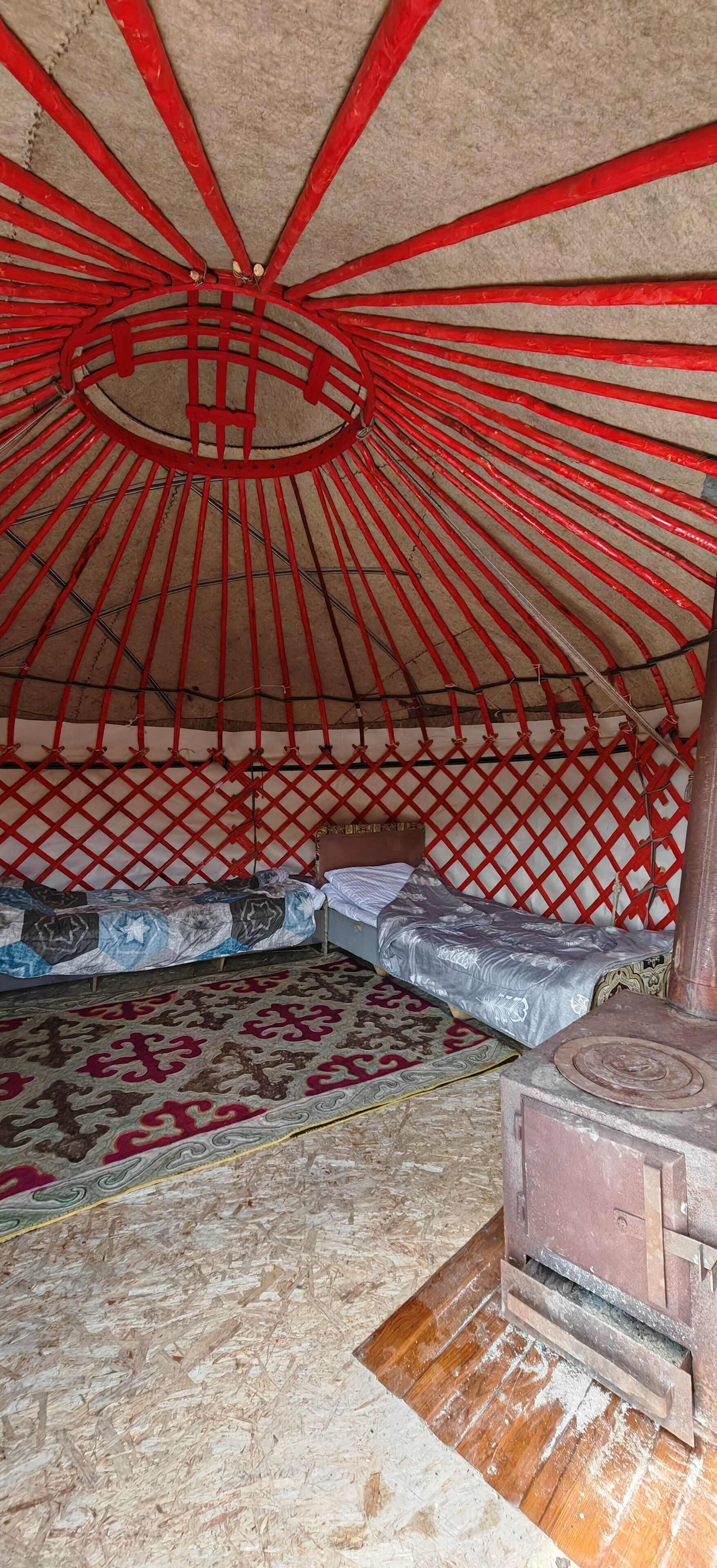 Interior de una yurta tradicional con estufa de madera, dos camas con ropa de cama estampada y una alfombra en el suelo.