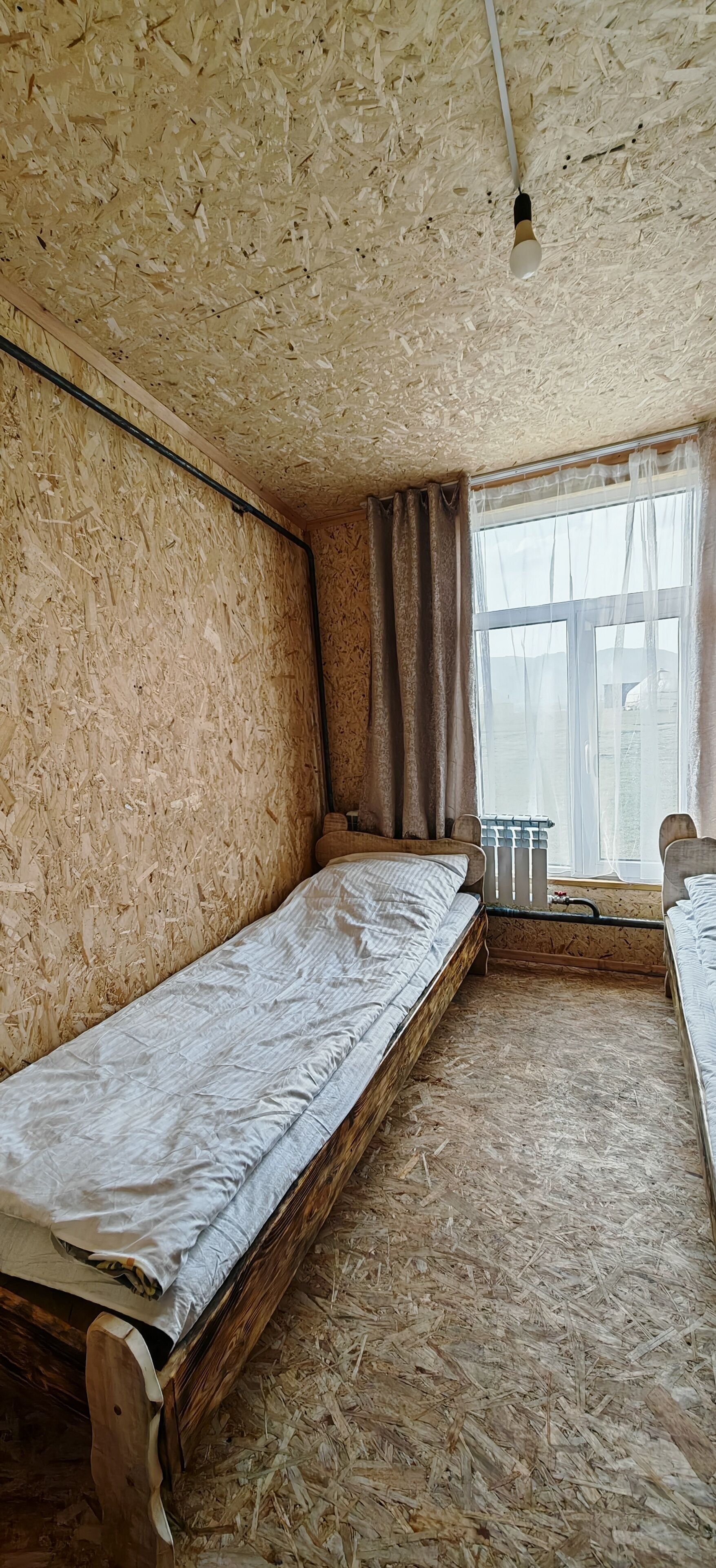 Une chambre avec deux lits superposés en bois, une fenêtre avec des rideaux et un radiateur.