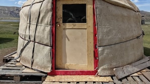 Une yourte avec une porte rouge, une cheminée et une plateforme en bois devant.