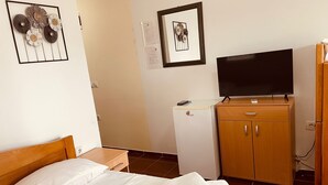 A hotel room with a bed, a TV on a wooden cabinet, a small refrigerator, and a wall with framed pictures. - Apartmens Sea House Dobra Voda (Dobre Vode)