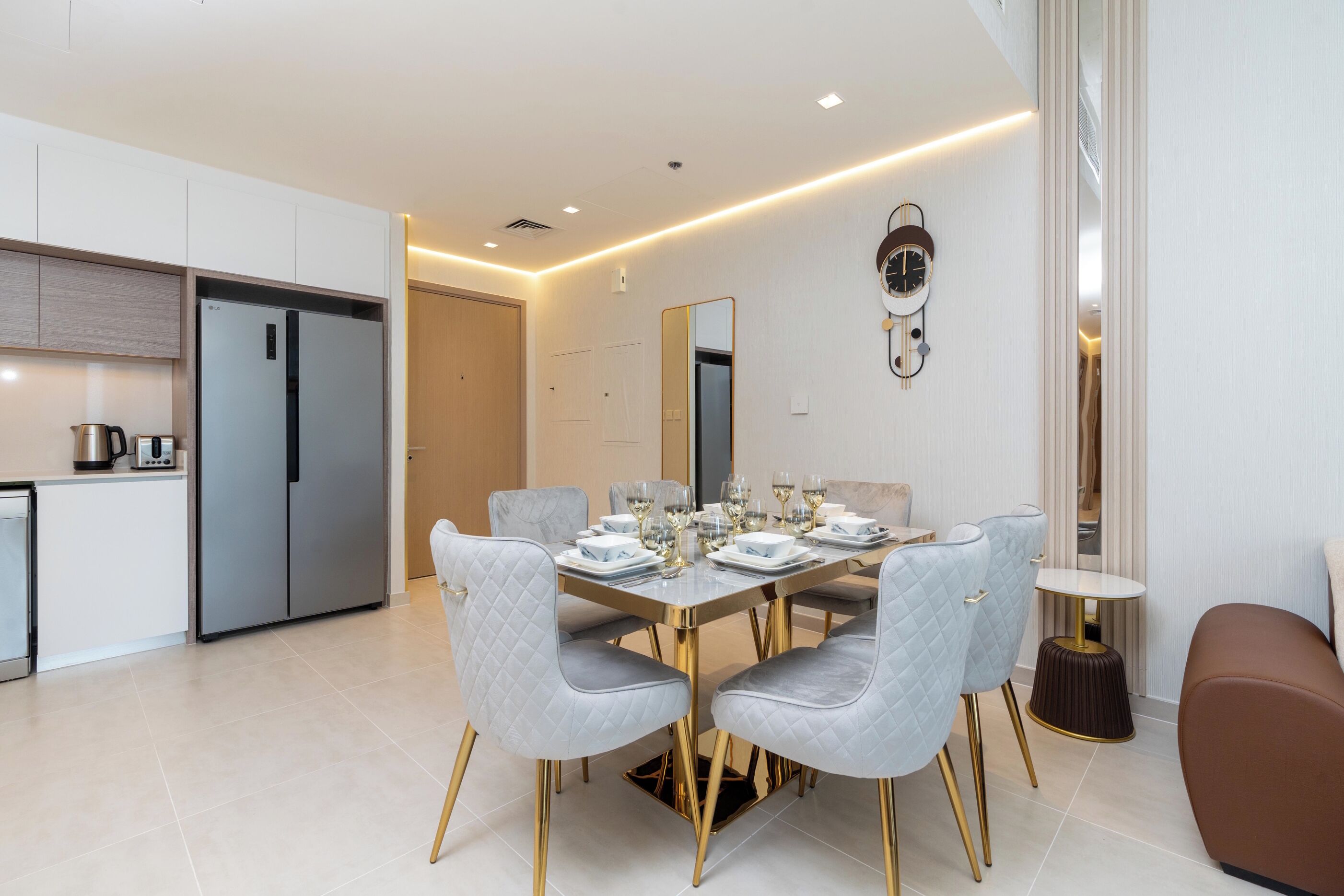 A modern dining area with a rectangular table set for four, surrounded by grey upholstered chairs with gold legs.