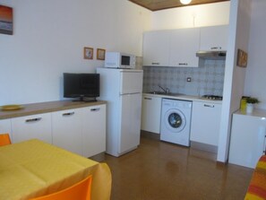 A compact kitchen with a washing machine, a microwave, and a small refrigerator. - Flat with big terrace in Grado (Grado Pineta)
