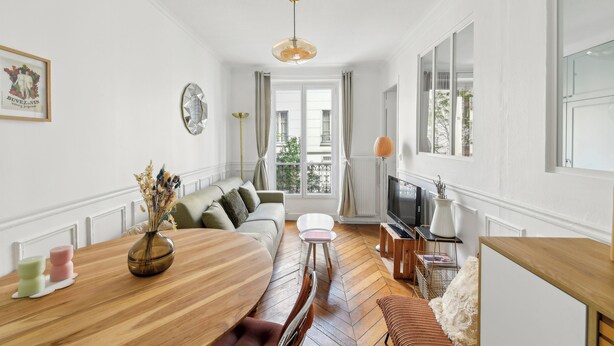 Uma sala de estar moderna com uma mesa de jantar de madeira, um sofá, uma TV e uma janela grande.