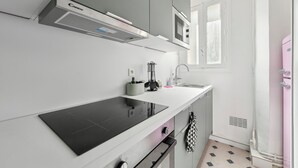 Uma cozinha moderna com um fogão por indução preto, armários cinzas, micro-ondas e uma geladeira rosa.