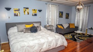 A bedroom with a large bed, a sofa, a nightstand, and a chandelier. - Downtown Cozy 2 BR Apt - 4min drive MardiGras Park (Mobile)