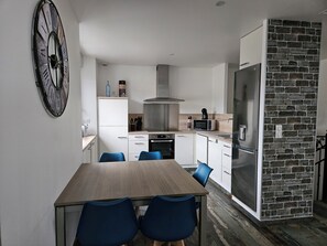 Une cuisine moderne avec des armoires blanches, une grande horloge et un mur d’accent en pierre.