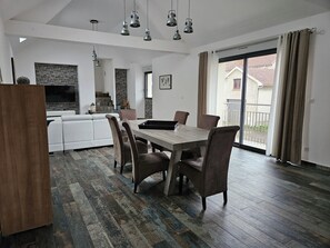 Une cuisine moderne avec un mur de fond en briques, un coin repas avec une table et des chaises en bois, et une porte-fenêtre coulissante donnant sur un balcon.