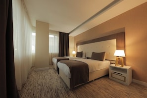 A hotel room with two beds, a nightstand with a lamp, a large window with curtains, and a patterned carpet. - VERA VISTA HOTEL (Van)