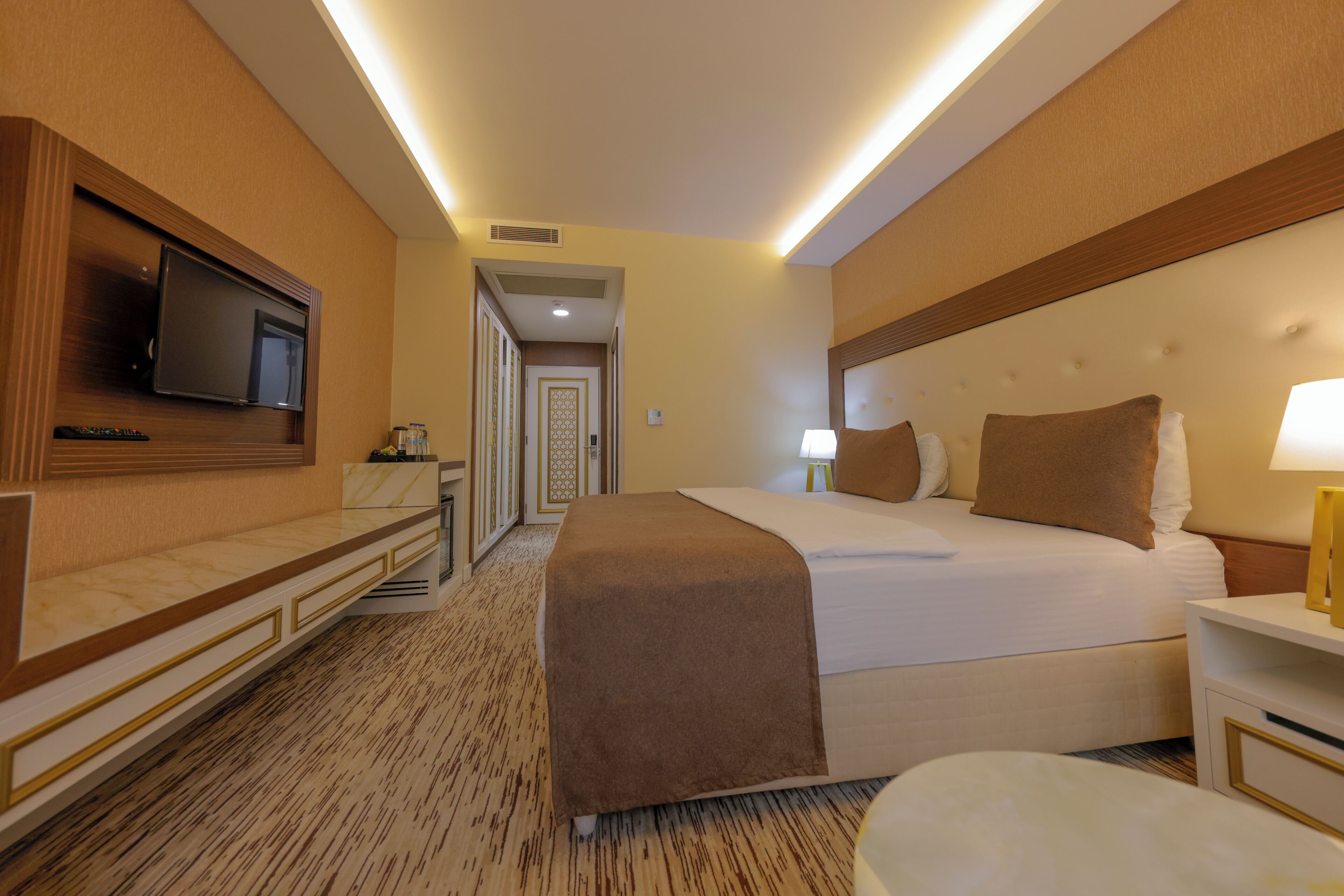 A hotel room with a bed, bedside table, TV, and a carpeted floor.