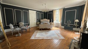 A bedroom with a large bed, two chairs, a table, and a chandelier.