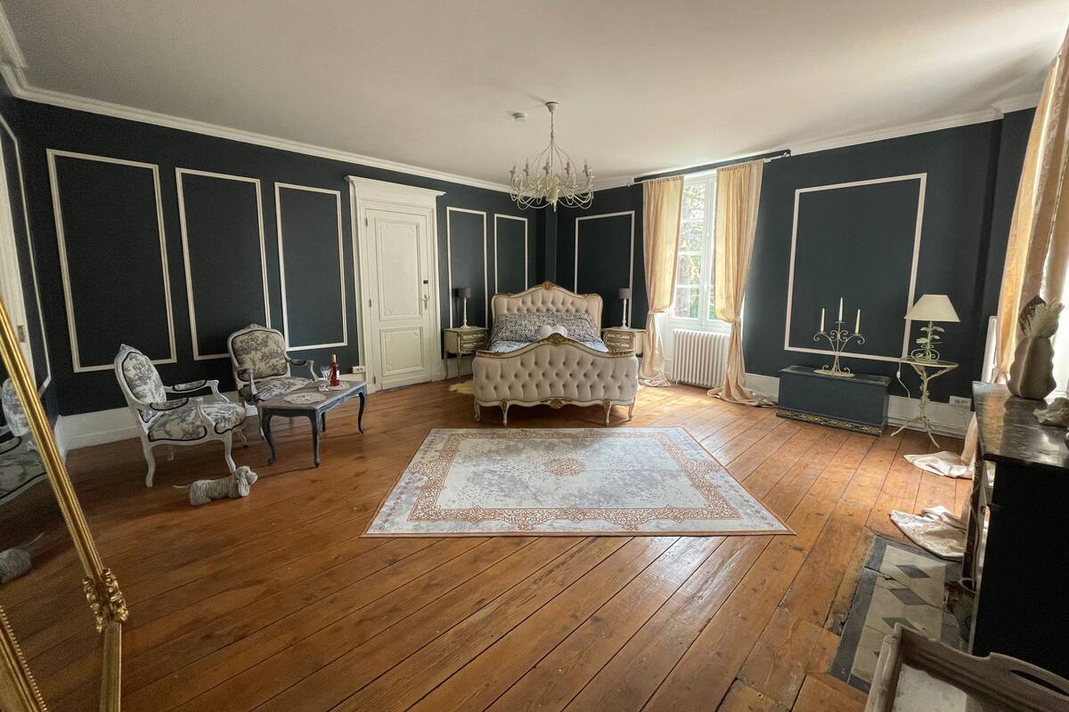 Une chambre à coucher avec un grand lit, deux fauteuils, une table et un lustre.