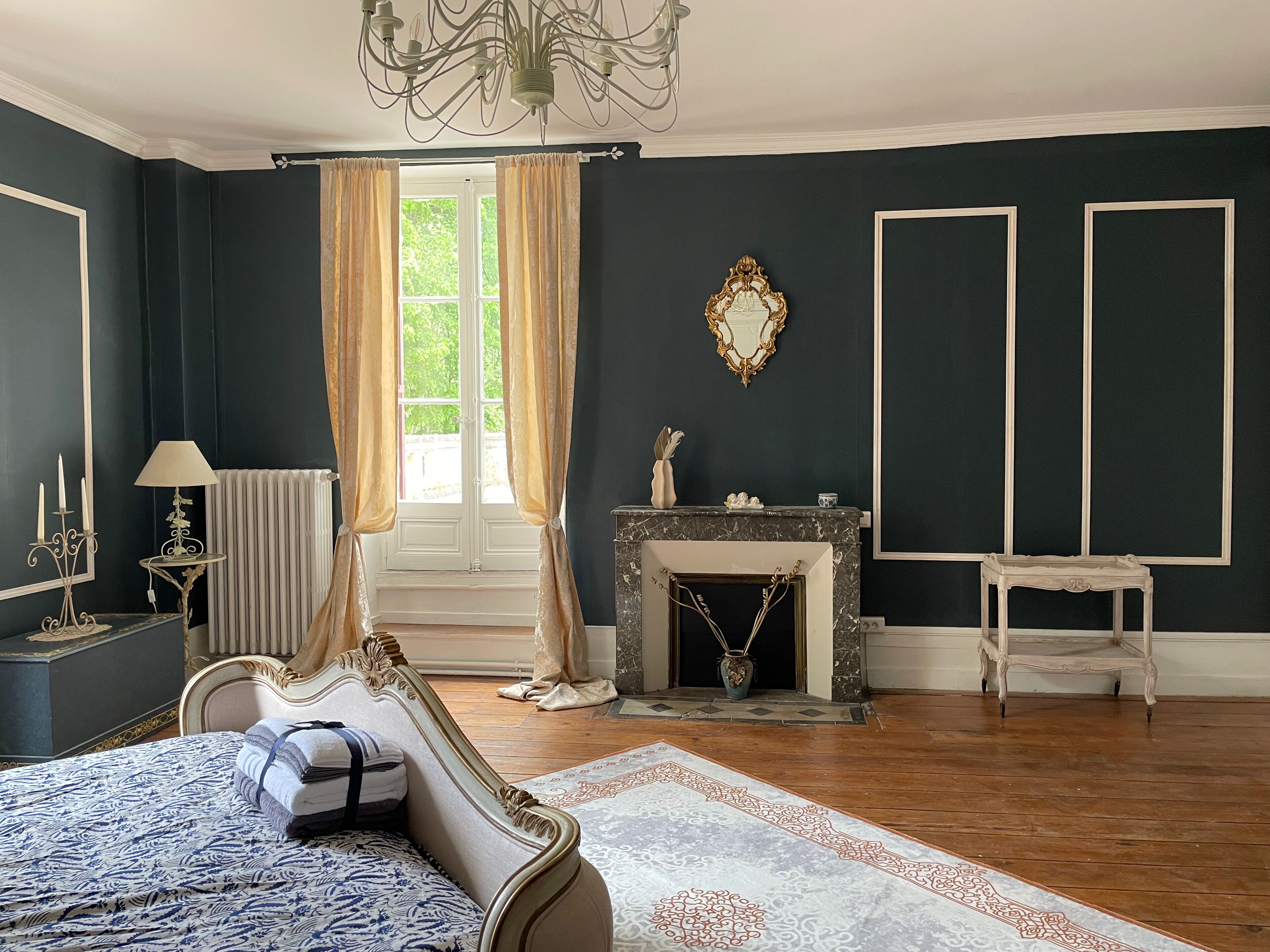 Une pièce comprenant un lit, une cheminée, un miroir et une fenêtre avec des rideaux.