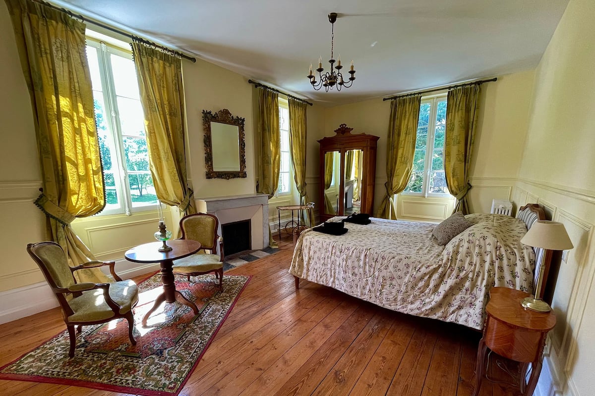 Une pièce comprenant un lit, une chaise, une table, un miroir et une cheminée.