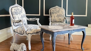 A room with two ornate chairs, a wooden table, and a bottle of red wine.