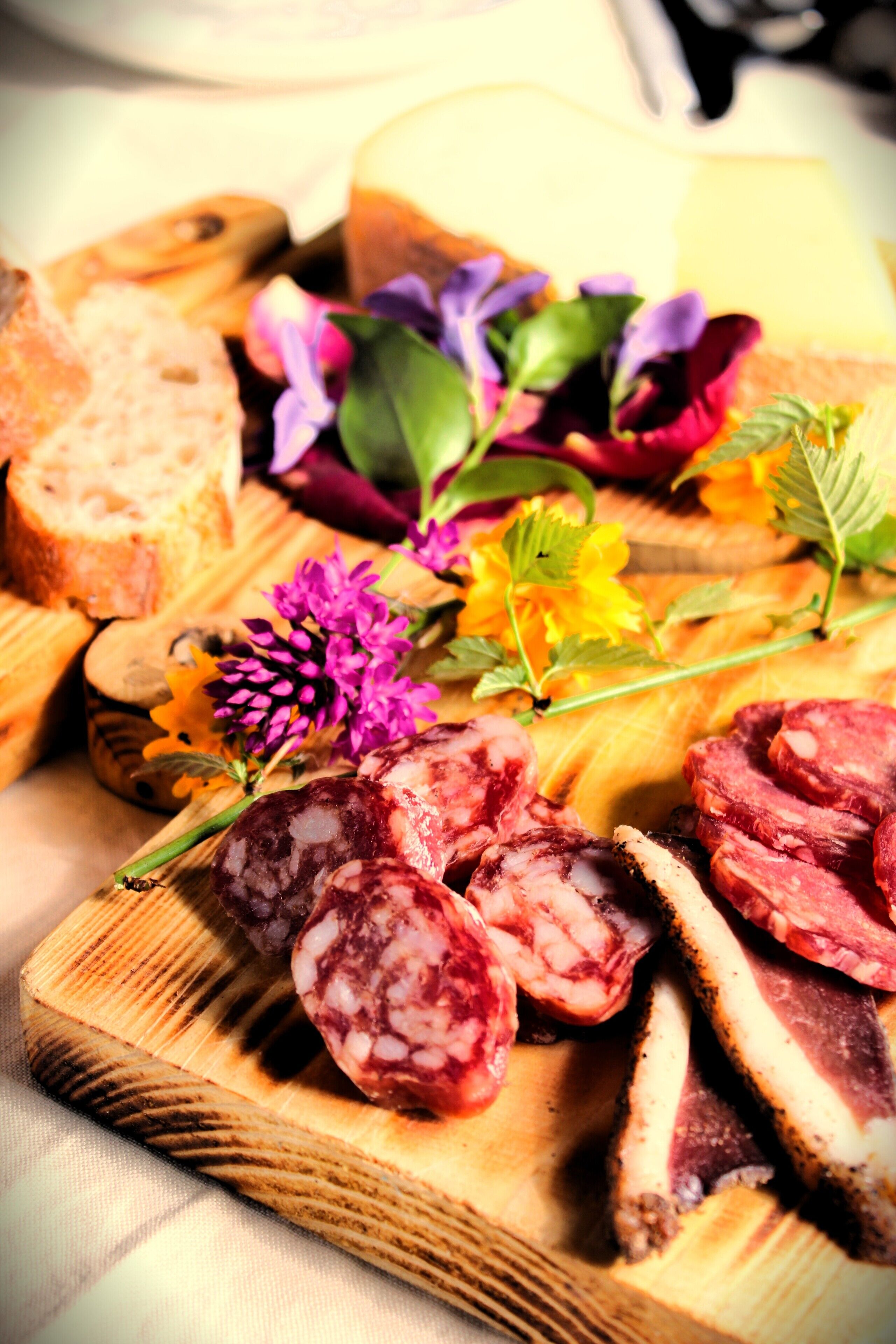 Une planche en bois garnie de tranches de salami, de pain et de fleurs.