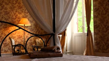 Een slaapkamer met een hemelbed, een nachtkastje met een lamp en bloemenbehang.