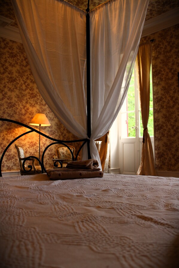 A bedroom with a canopy bed, a bedside table with a lamp, and floral wallpaper.