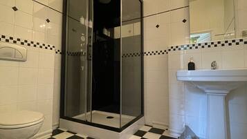 A bathroom with a glass-enclosed shower, a white toilet, and a sink with a mirror above it. The floor has a black and white checkered pattern.