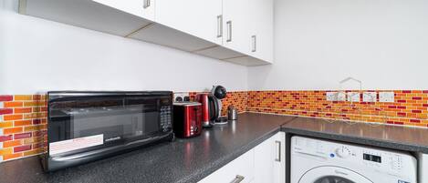 Una cocina con gabinetes blancos, microondas, tostadora y lavadora.