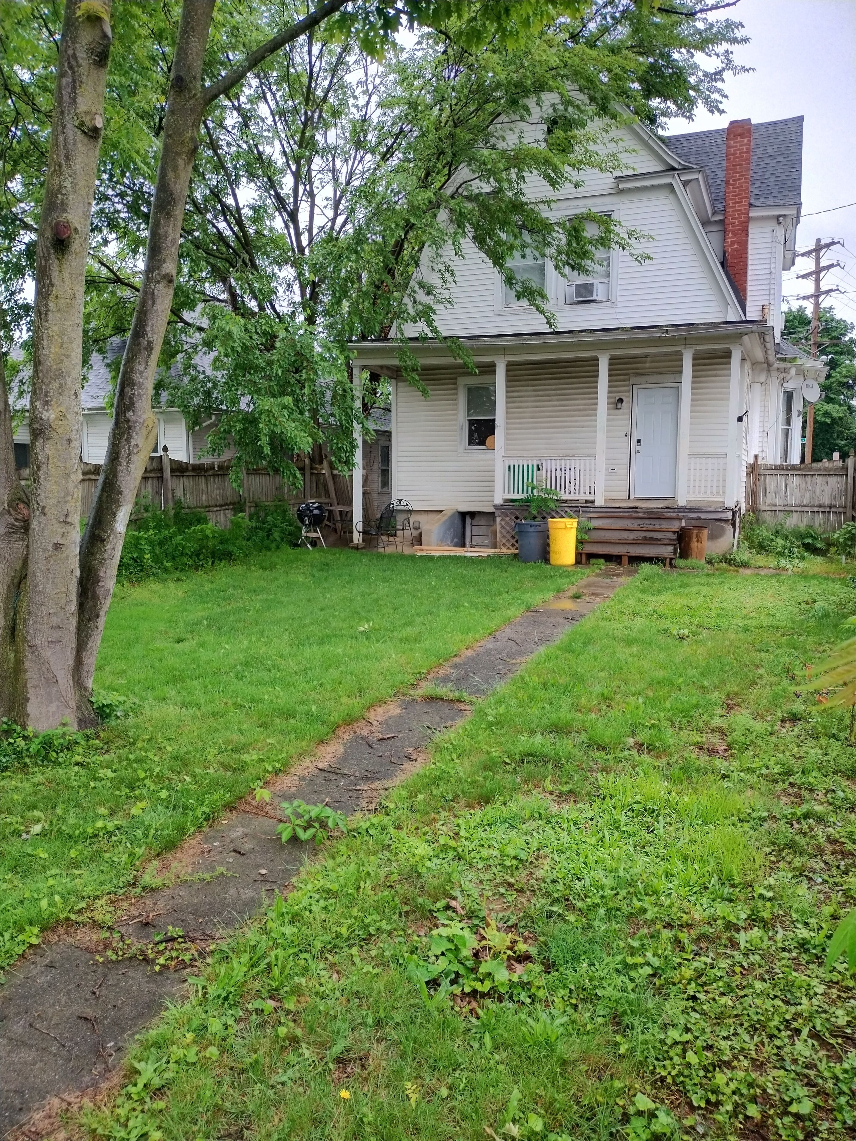 A two-story house with a front porch, a visible chimney, and a fenced backyard.