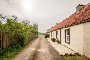 A rural road leading to a row of traditional houses with red-tiled roofs and white walls. - Jura Cottage | Peat Inn (Peat Inn)