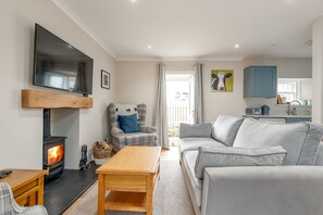 A cozy living room with a fireplace, a sofa, a chair, and a television mounted on the wall. - Jura Cottage | Peat Inn (Peat Inn)