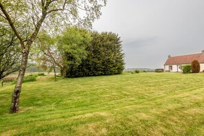 A grassy field with a large tree and a building with a red roof. - Jura Cottage | Peat Inn (Peat Inn)