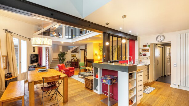 Ein geräumiger Wohnbereich mit einem Holzesstisch, einem roten Sofa und einer Küchenzeile mit Bar.