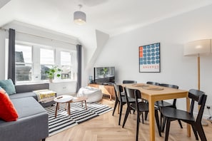 Un salon moderne avec un canapé, une table basse et une table à manger avec des chaises. On y trouve également un téléviseur et une plante sur le rebord de la fenêtre.