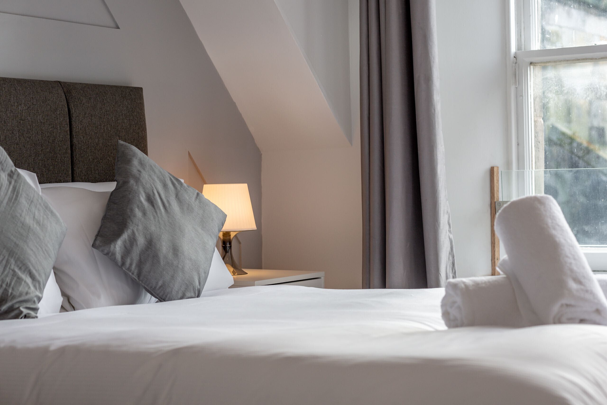 A hotel room with a neatly made bed, a bedside lamp, and a window with curtains.