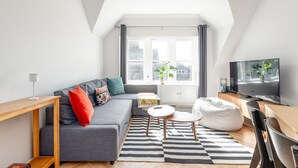 A modern living room with a grey sofa, a wooden coffee table, a striped rug, a television, and a potted plant. - Spire View Apartment (St Andrews)