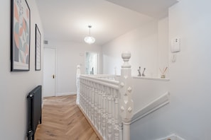 Un couloir avec une rambarde blanche, un radiateur et une porte au fond.