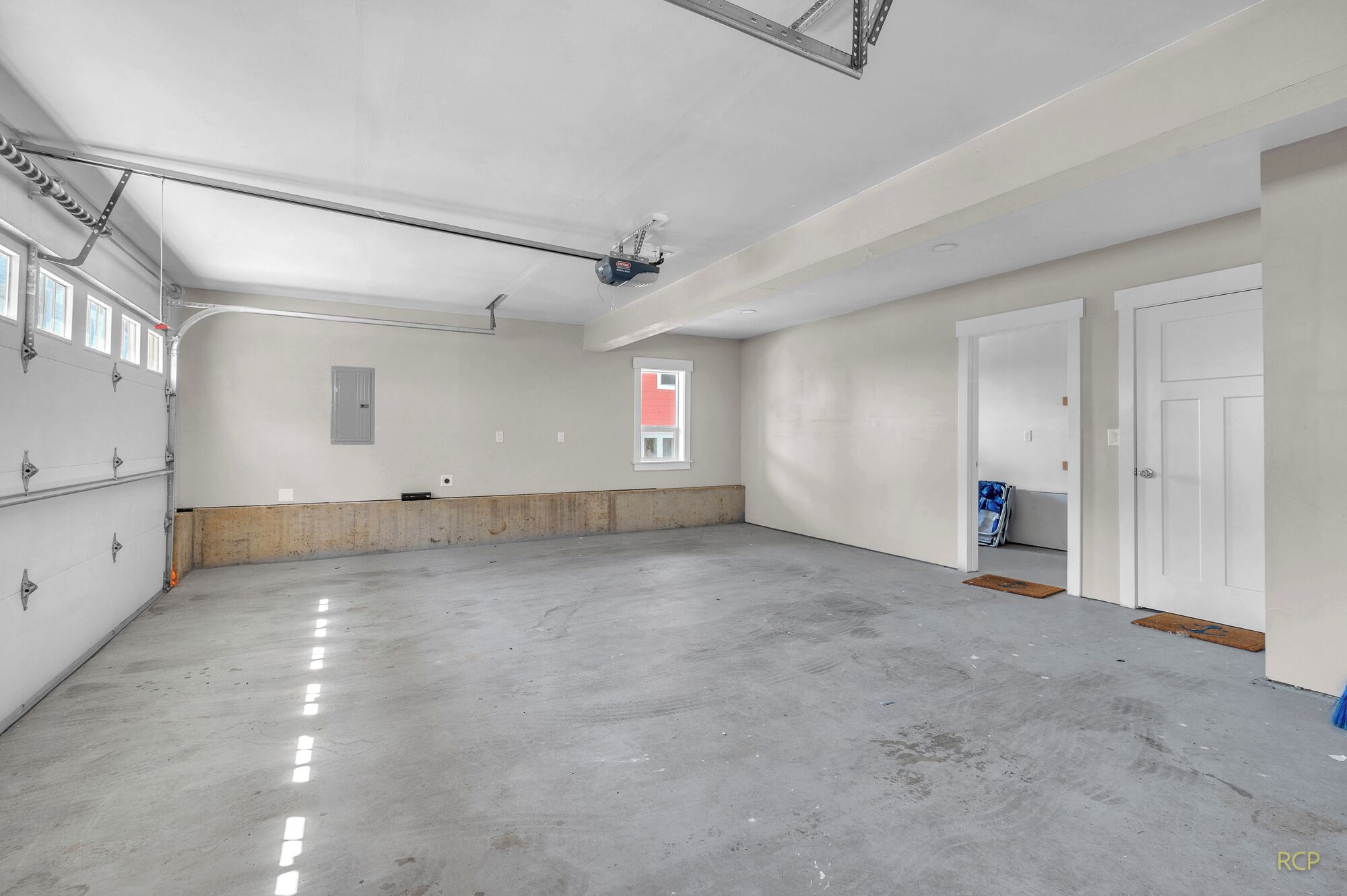 A spacious, unfinished garage with concrete floors, a high ceiling, and a large window.