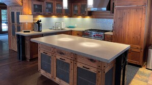 A modern kitchen with wooden cabinets, a central island, stainless steel appliances, and pendant lighting. - 4-bedroom cabin Chalet Nestled in the Sundance Mountains (Provo)