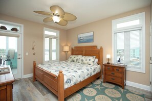 Une chambre à coucher avec un lit en bois, un ventilateur de plafond, une table de chevet et une vue sur l’extérieur.