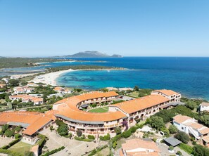 Un complejo turístico costero con un edificio curvo, acceso directo a la playa y vistas al mar y a islas distantes.