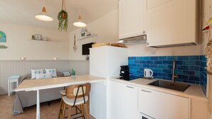 Een moderne keuken met witte kasten, een blauw betegelde achterwand, een koffieapparaat en een hangplant.