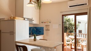 Een compacte keuken met een centraal eiland, een eethoek met stoelen en een glazen schuifdeur naar een terras.