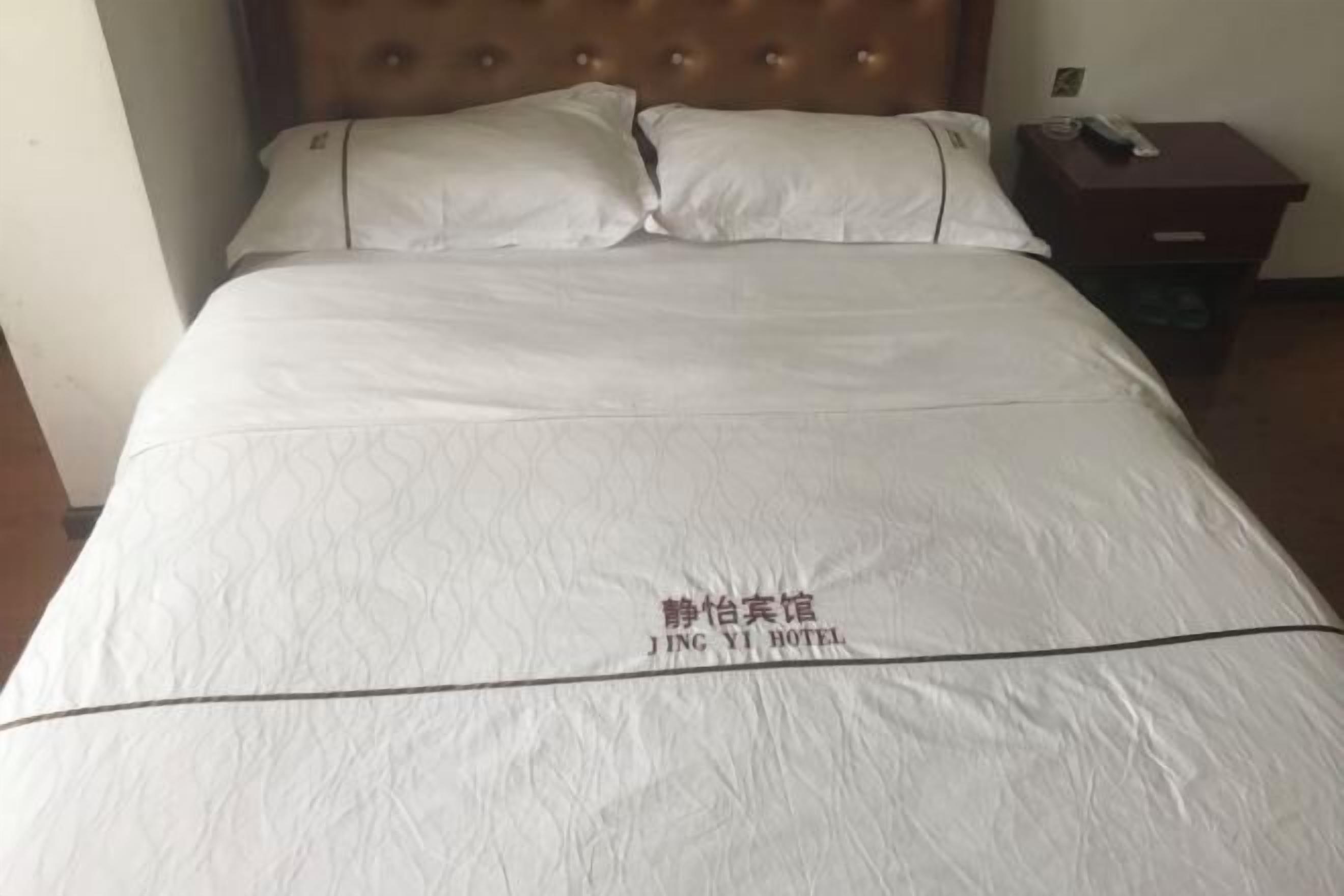 A bed with a white bedspread and pillows, a wooden headboard, and a nightstand with a remote control.