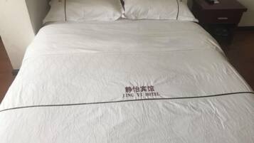 A bed with a white bedspread and pillows, a wooden headboard, and a nightstand with a remote control.