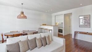 A modern living room with a white sofa, a dining table, and a kitchen in the background. - Casas do Rivoli (Porto)