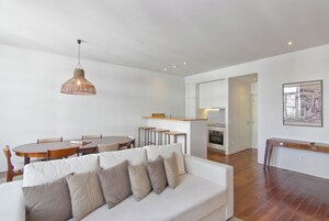 Una sala de estar moderna con un sofá blanco, una mesa de comedor y una cocina al fondo.